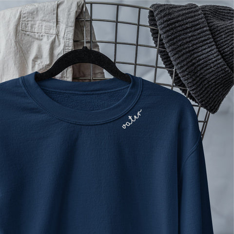 3. Close-up of navy unisex sweatshirt with light gray 'Vater' embroidery on collar, hanging on wire basket