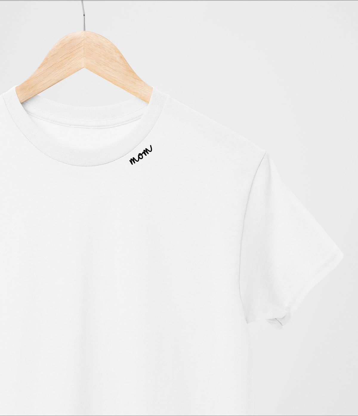 2. White organic cotton t-shirt with 'mom' embroidery on hanger in studio