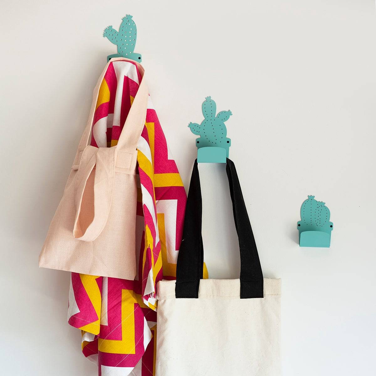 1. Set of three cactus-shaped metal hangers in blue, holding colorful bags and towels against a white wall