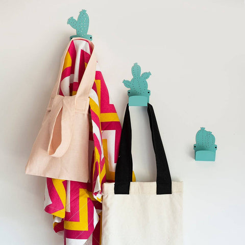 1. Set of three cactus-shaped metal hangers in blue, holding colorful bags and towels against a white wall