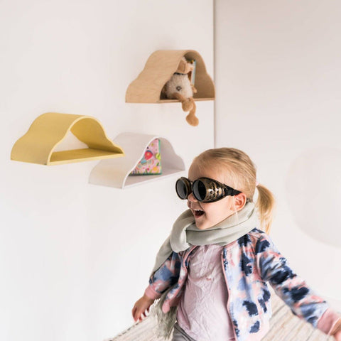 4. Child wearing sunglasses and scarf in front of three cloud-shaped floating shelves in white, yellow, and natural wood colors.