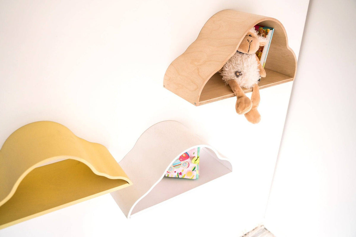 1. Three cloud-shaped floating shelves in white, yellow, and natural wood colors on a wall, holding a stuffed toy and a book, in a child's room.