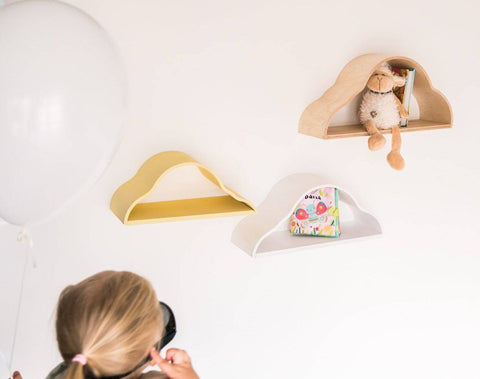 5. Child with balloon looking at three cloud-shaped floating shelves in white, yellow, and natural wood colors on a wall.