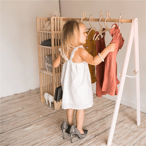 1. Young girl in white dress using Ewart Woods kids wooden clothing rack with pink frame in a cozy room setting