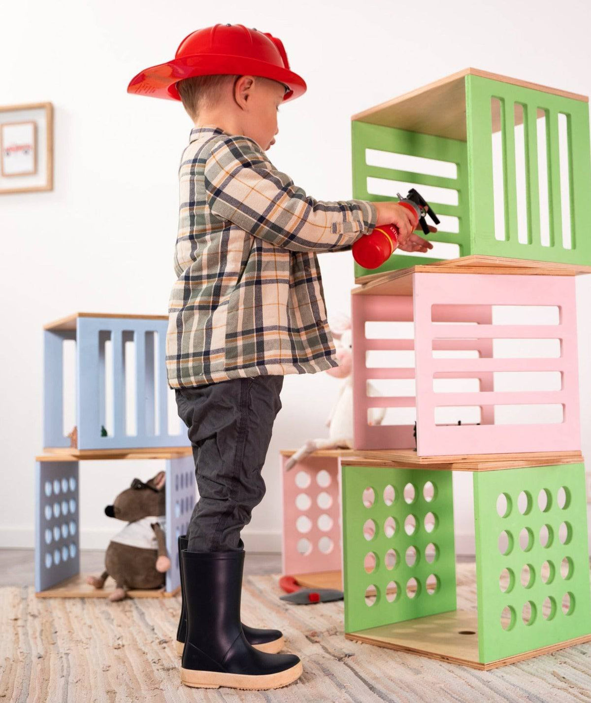 4. Side view of child in plaid shirt and red hat playing with stacked Ewart Woods storage cubes