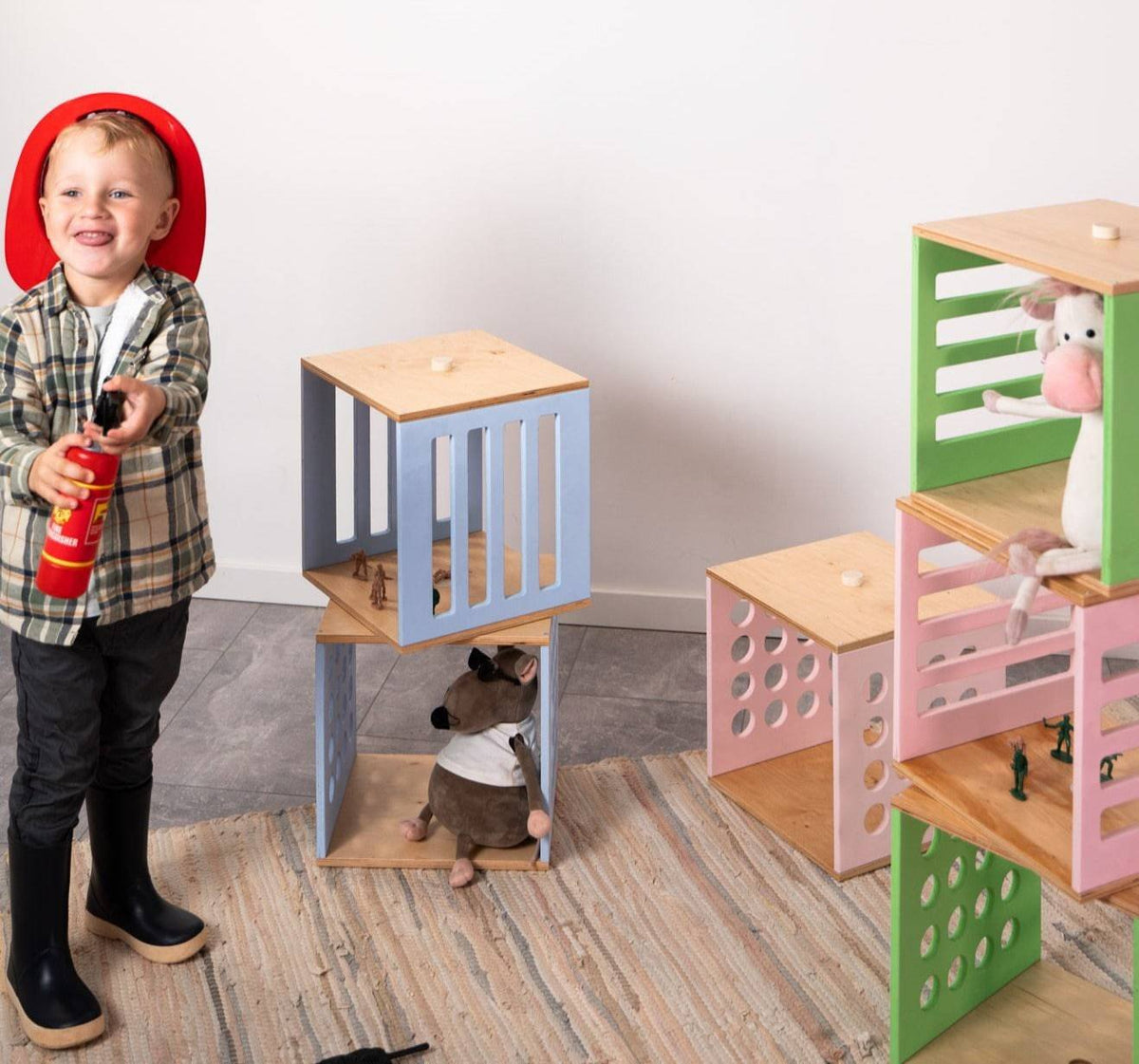 1. Child wearing red firefighter hat playing with colorful Ewart Woods toy storage cubes in a room setting