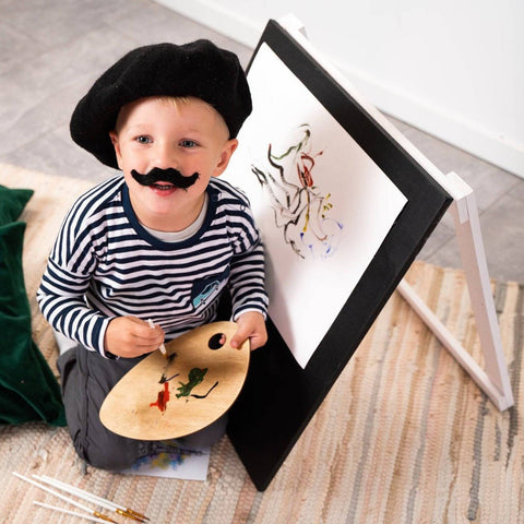 5. Child in striped shirt and beret smiling while painting on Ewart Woods black wooden chalkboard easel