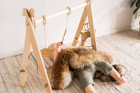 1. Baby lying under wooden play gym with Viking-themed toys on a textured rug