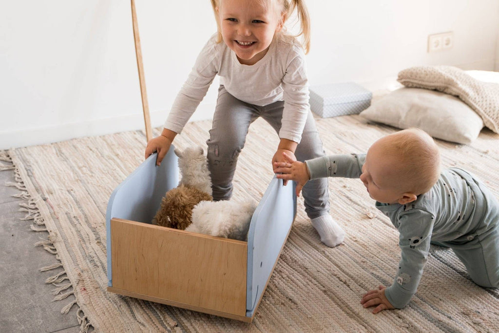 6. Child pushing blue whale-shaped wooden toy box on wheels with baby nearby