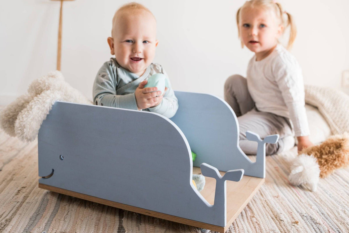 1. Two children playing with blue whale-shaped wooden toy box on wheels in a cozy room