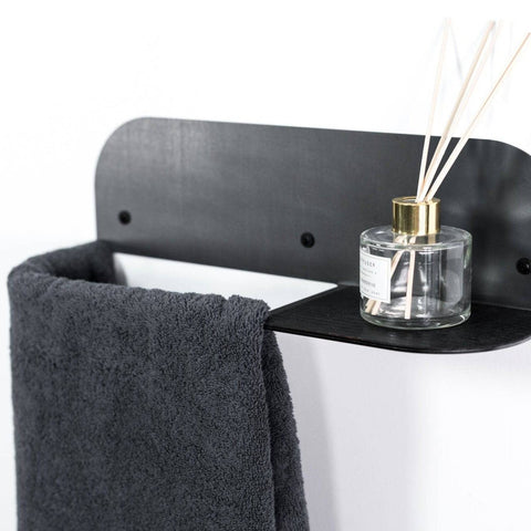 1. Wall-mounted steel and wood towel rack with black finish, holding a dark towel and a glass diffuser on a small shelf, against a white background
