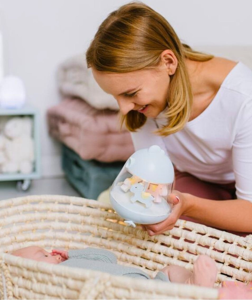 1. Woman holding blue Rabbit & Friends lamp with carousel over baby in basket