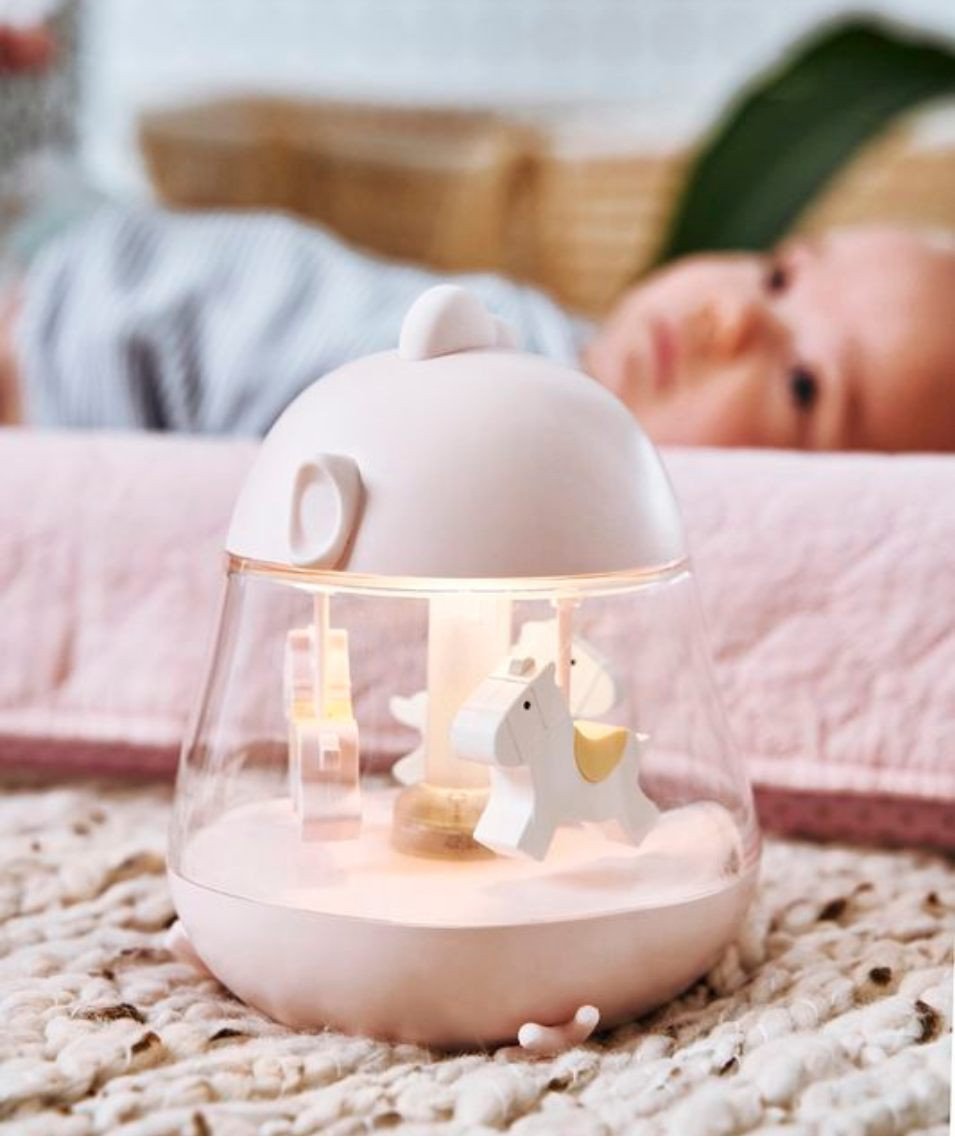 1. Baby lying on a blanket with a pink Rabbit & Friends lamp with carousel and music box nearby