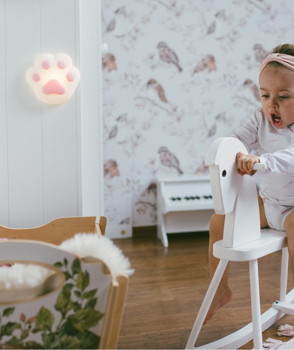 5. Child riding white rocking horse with pink paw-shaped silicone lamp on wall in playroom
