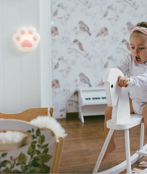 5. Child riding white rocking horse with pink paw-shaped silicone lamp on wall in playroom
