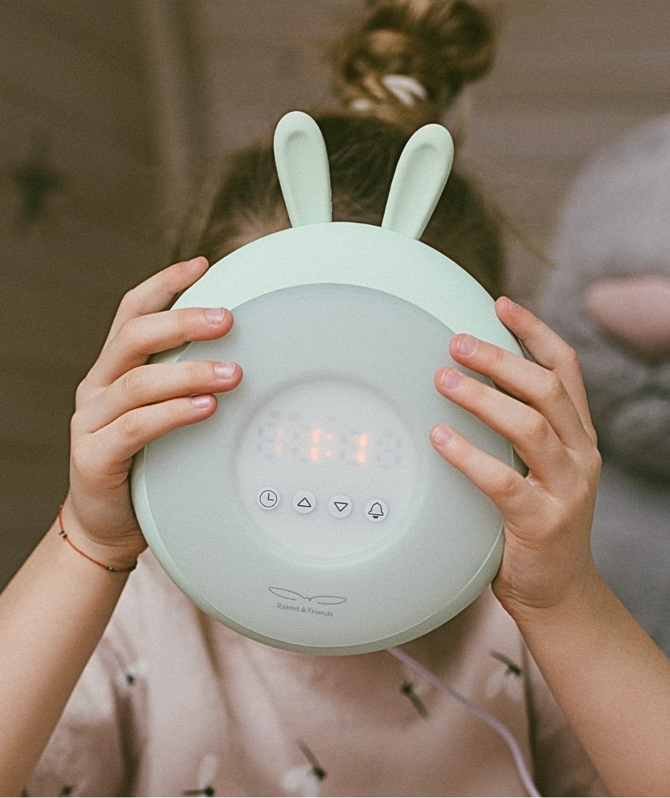1. Child holding green Rabbit & Friends lamp with alarm clock, showing digital display and rabbit ears in cozy room setting