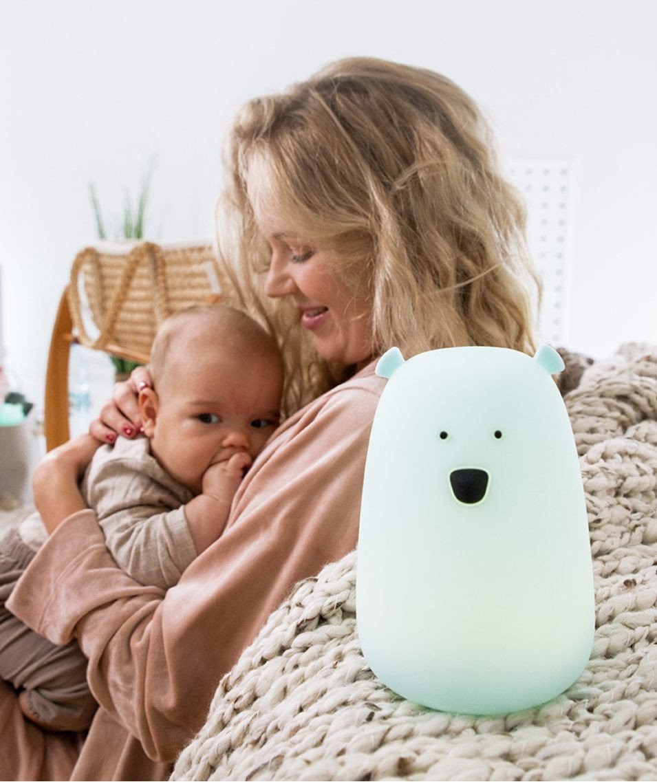 1. Woman holding baby with blue teddy bear lamp on bed