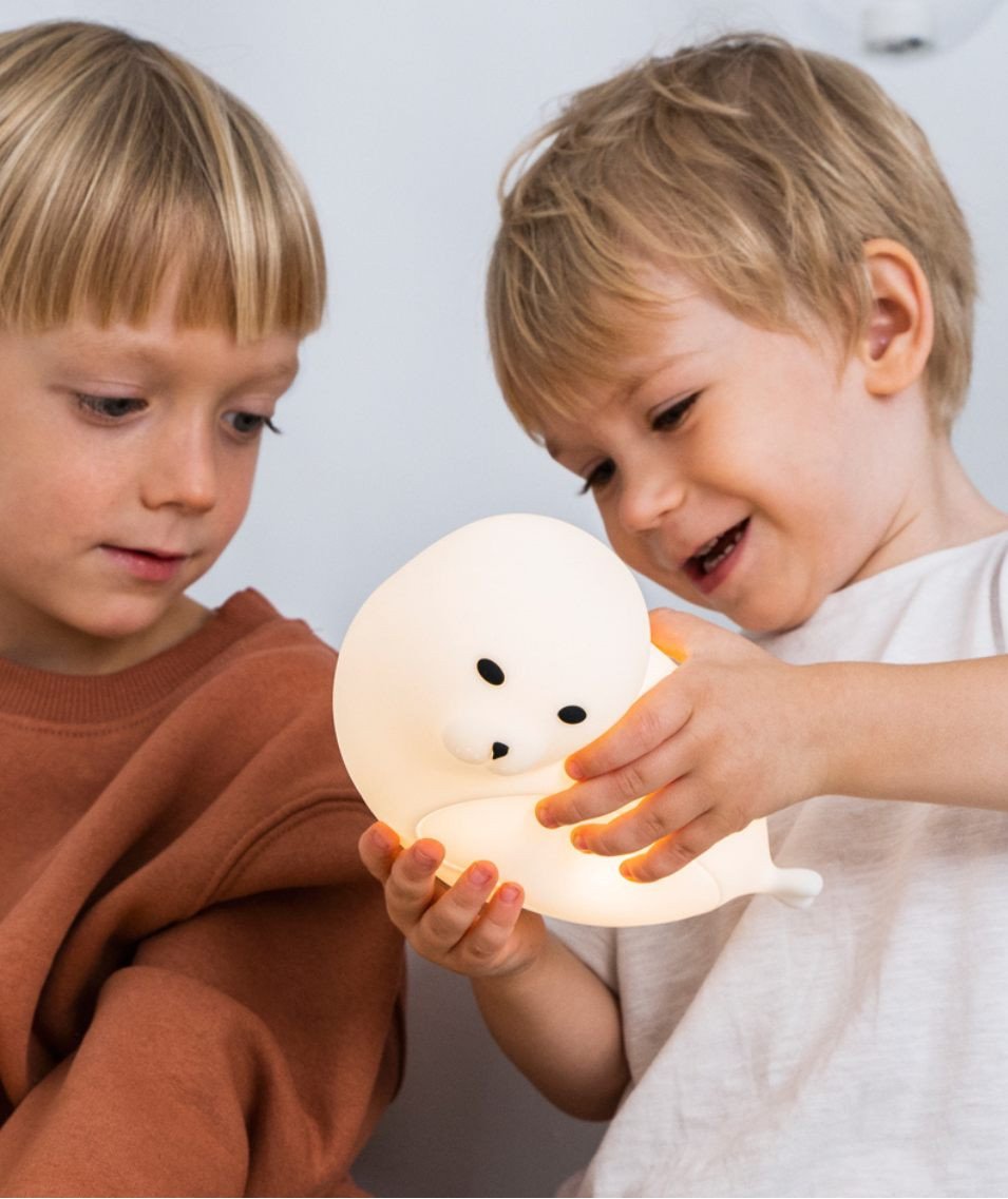 1. Two children playing with glowing white seal-shaped lamp indoors