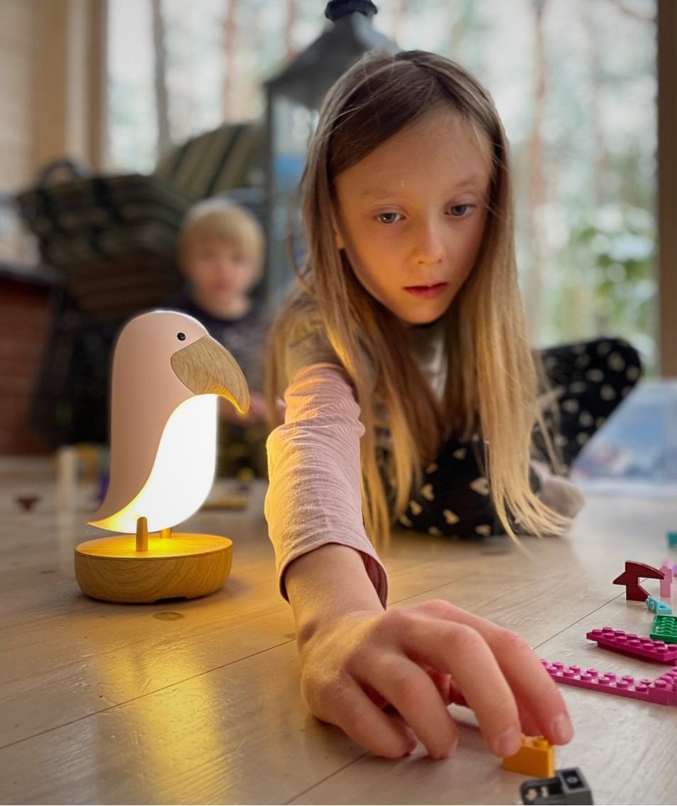 1. Girl playing on floor with pink bird lamp glowing beside her, creating a cozy play environment