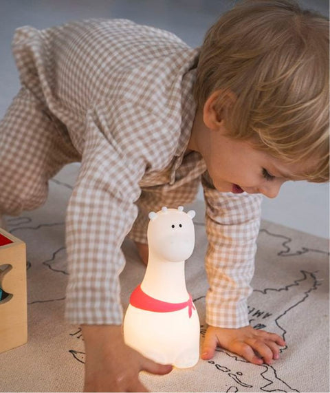 1. Child playing with glowing white silicone giraffe lamp with red scarf on floor