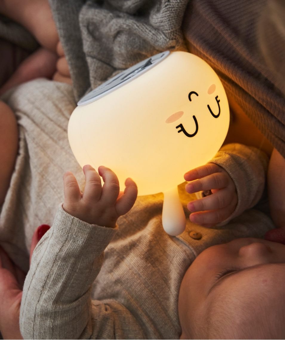 6. Baby holding glowing white Bunny Silicone Lamp while lying on a bed