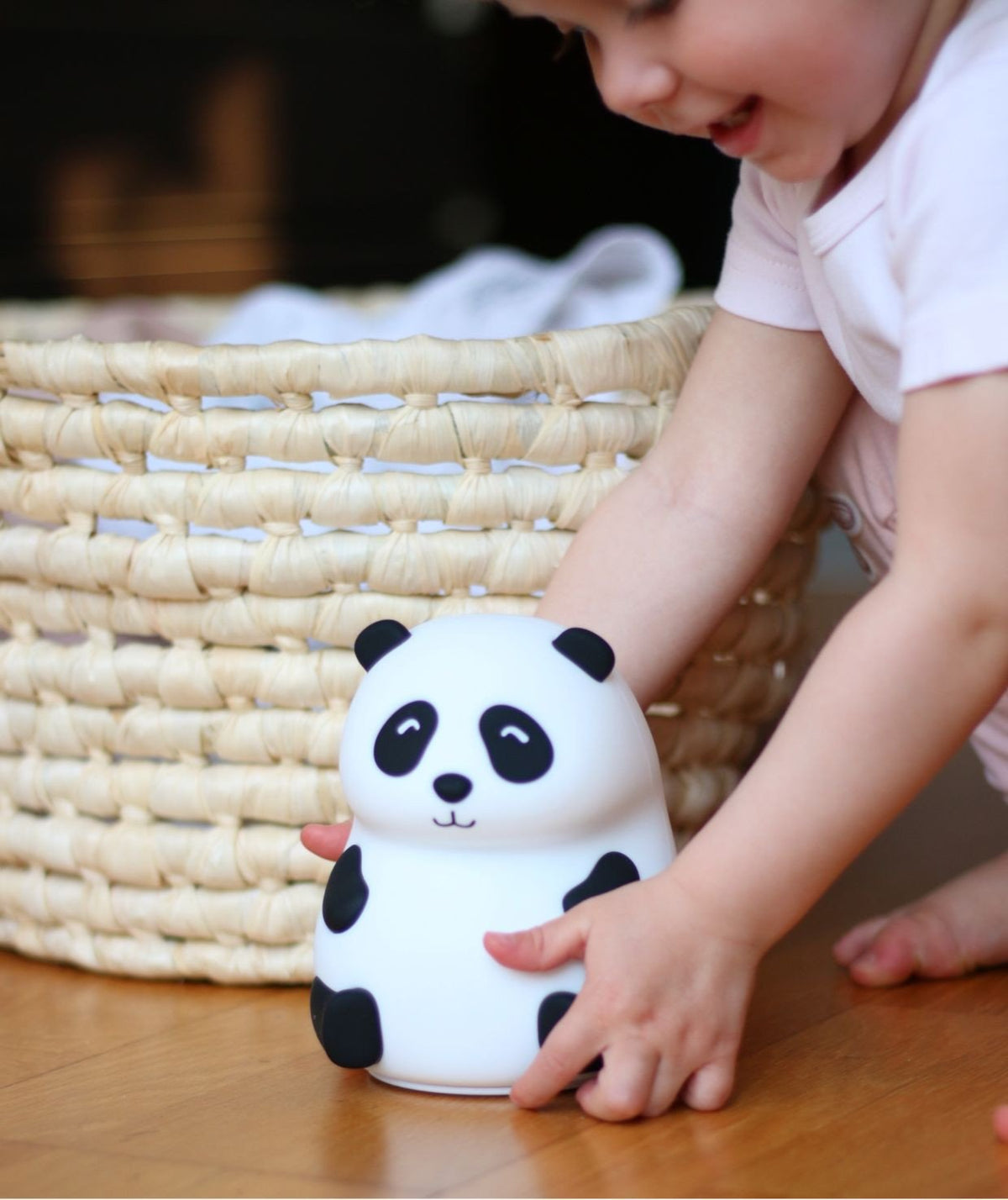 1. Child playing with Rabbit & Friends panda silicone lamp on wooden floor next to woven basket