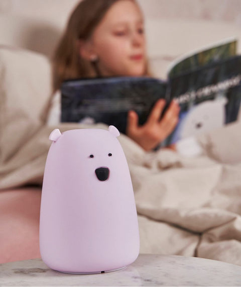 1. Girl reading a book in bed with a lavender Big Bear silicone lamp by Rabbit & Friends on the bedside table