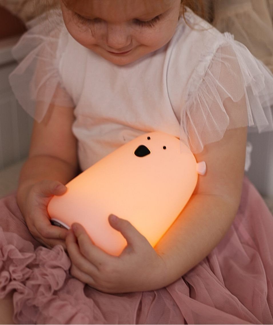 1. Child holding a glowing lavender Big Bear silicone lamp by Rabbit & Friends, wearing a pink skirt and white top