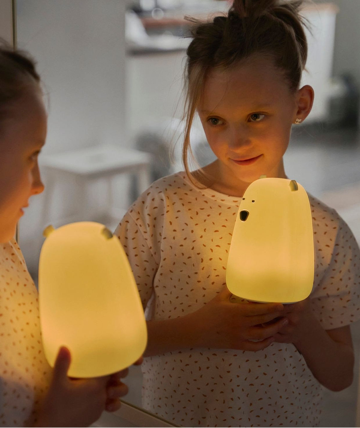 1. Young girl holding a glowing Big Bear silicone lamp by Rabbit & Friends, smiling at her reflection in a mirror