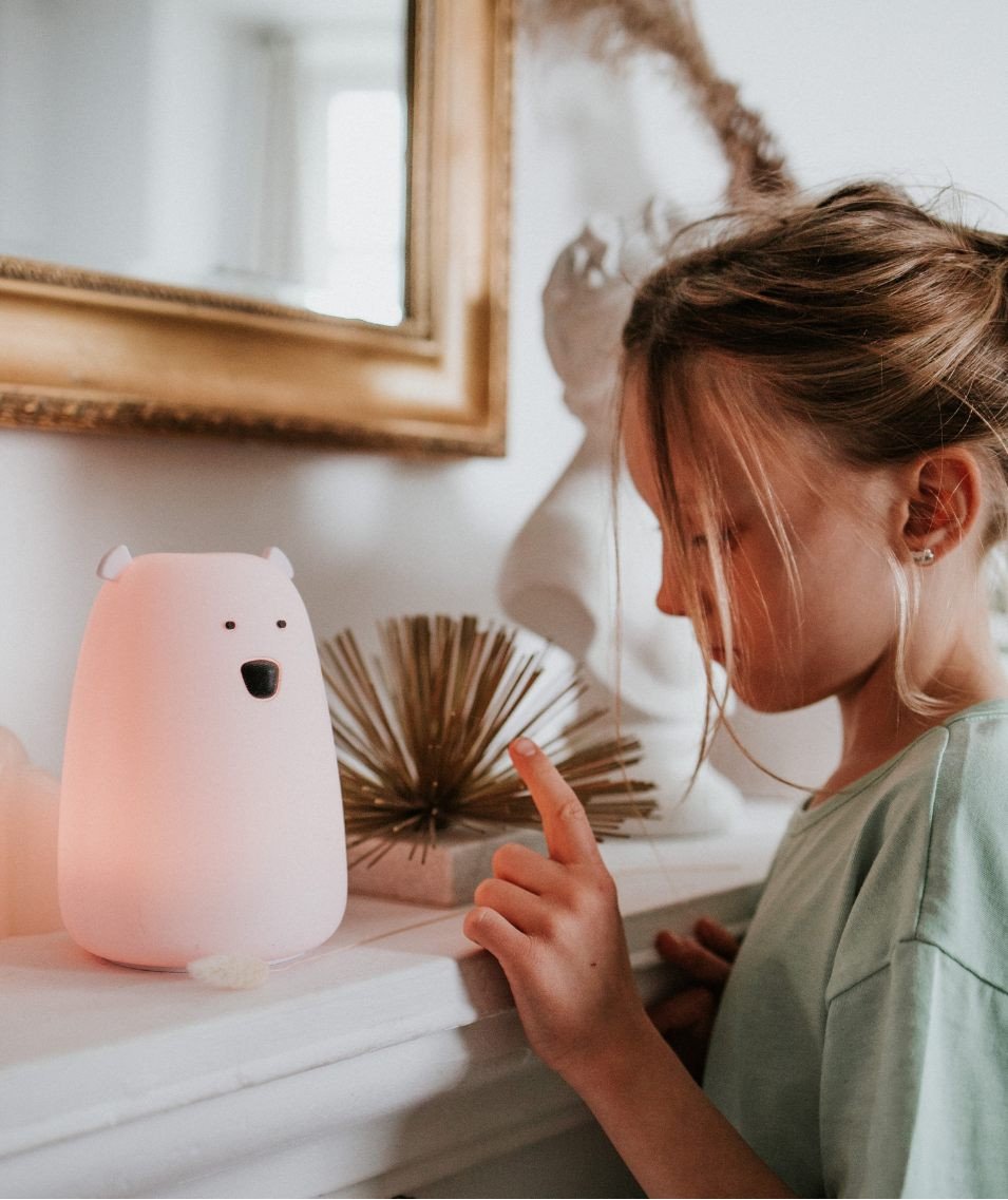 1. Girl interacting with glowing pink bear lamp on mantelpiece