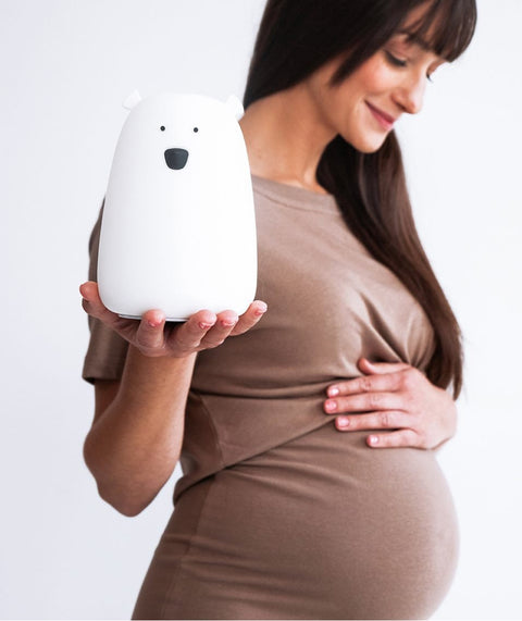 1. Pregnant woman in brown dress holding a white Big Bear silicone lamp by Rabbit & Friends, smiling gently