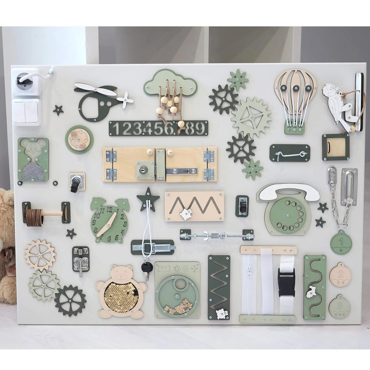 4. Flat lay of Montessori sensory busy board in green and beige, showcasing various interactive elements for skill development.