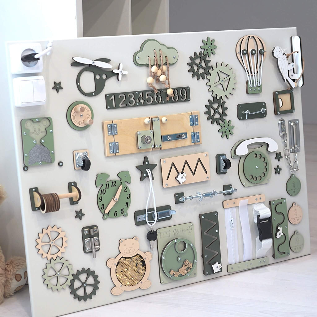 6. Close-up of green and beige Montessori busy board, featuring interactive elements for sensory and motor skill development, shown in a minimalist room.