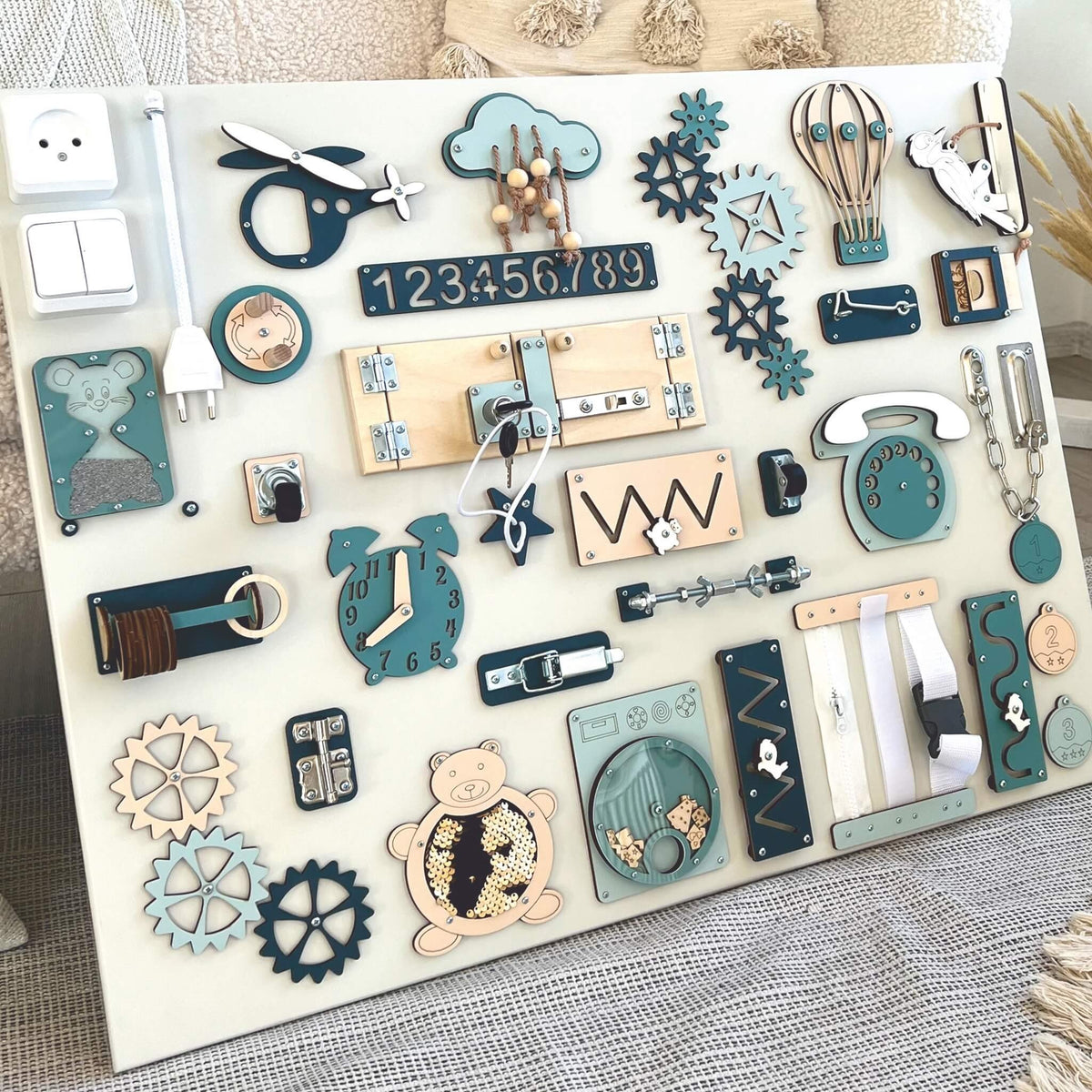 3. Close-up of Montessori busy board with blue and beige elements, highlighting interactive features for sensory play, set against a soft fabric background.