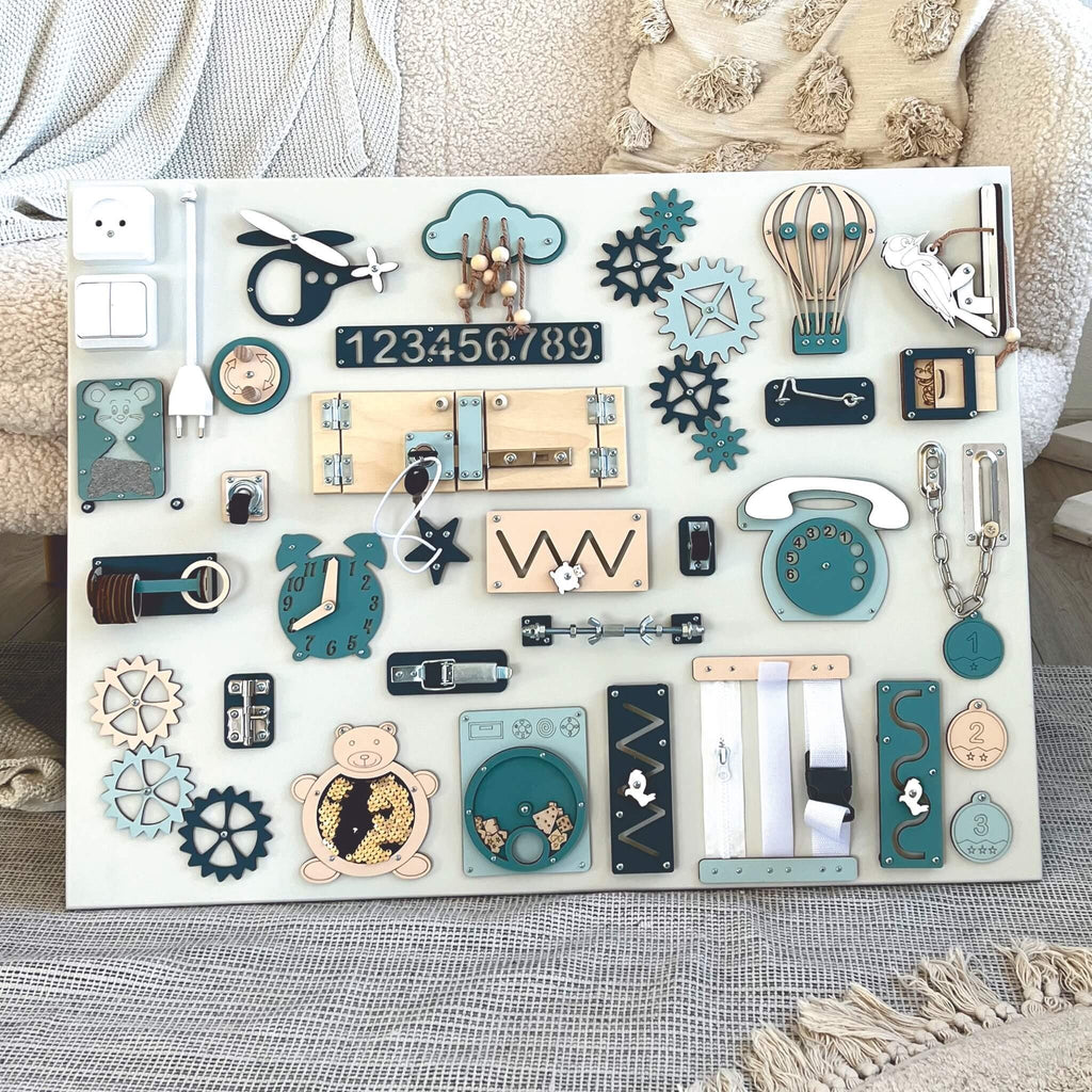 2. Montessori sensory busy board in blue and beige, featuring interactive elements for motor skills, placed on a cozy sofa with textured cushions.