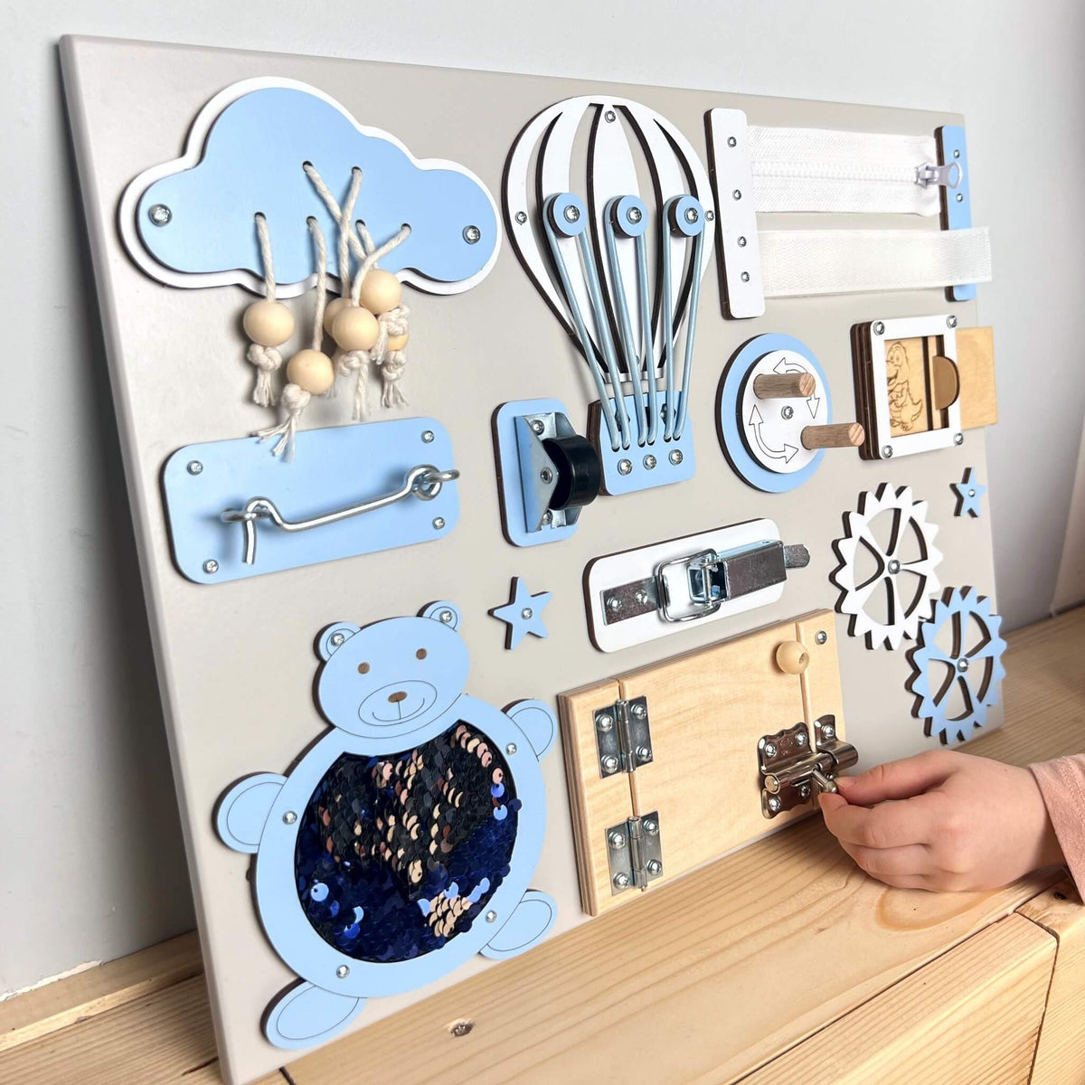 4. Child's hand interacting with blue and natural wood busy board featuring doors and gears