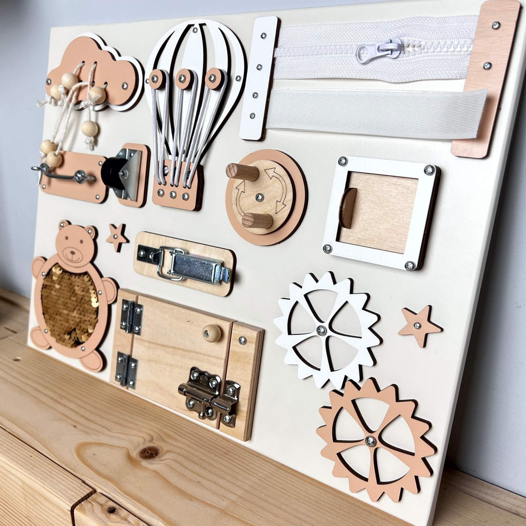 5. Peach and natural wood busy board with interactive elements, displayed on a wooden surface