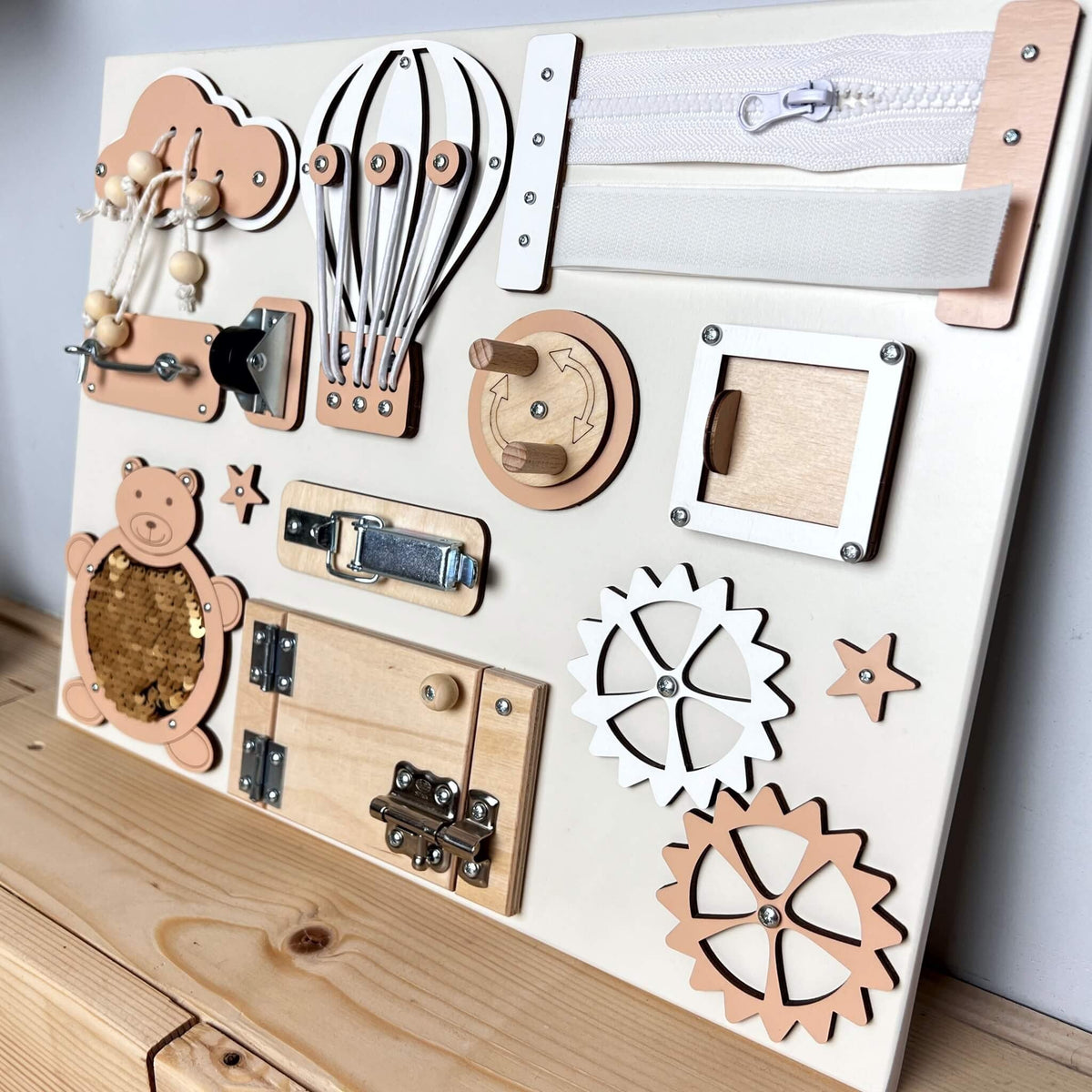 5. Peach and natural wood busy board with interactive elements, displayed on a wooden surface