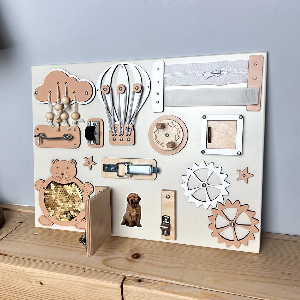 6. BusyBunnyToys busy board in peach tones with interactive elements and a small door revealing a dog image