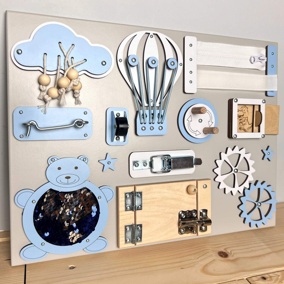 1. Extra small busy board with blue and natural wood elements, featuring interactive doors and gears, on a wooden surface