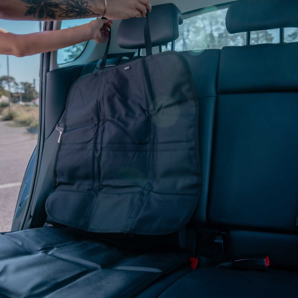 2. Ezi Mat 3 in 1 seat protector being installed on rear car seat, showing adjustable straps