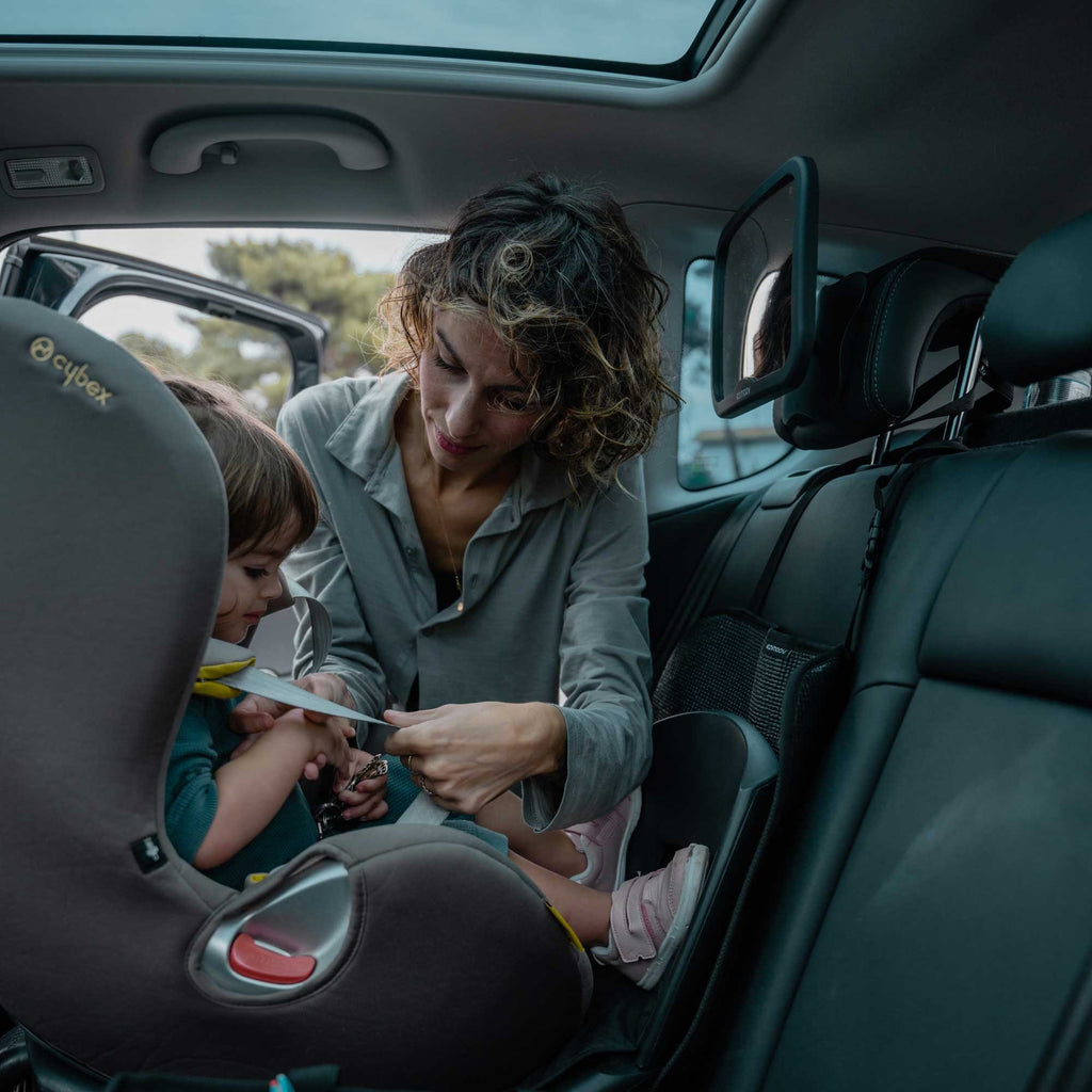 3. Woman adjusting child's seatbelt in car with Ezimoov EZI MIRROR SQUARE visible, demonstrating ease of use