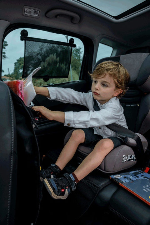 1. Child in car seat with Ezimoov sunshade on window, reaching for book