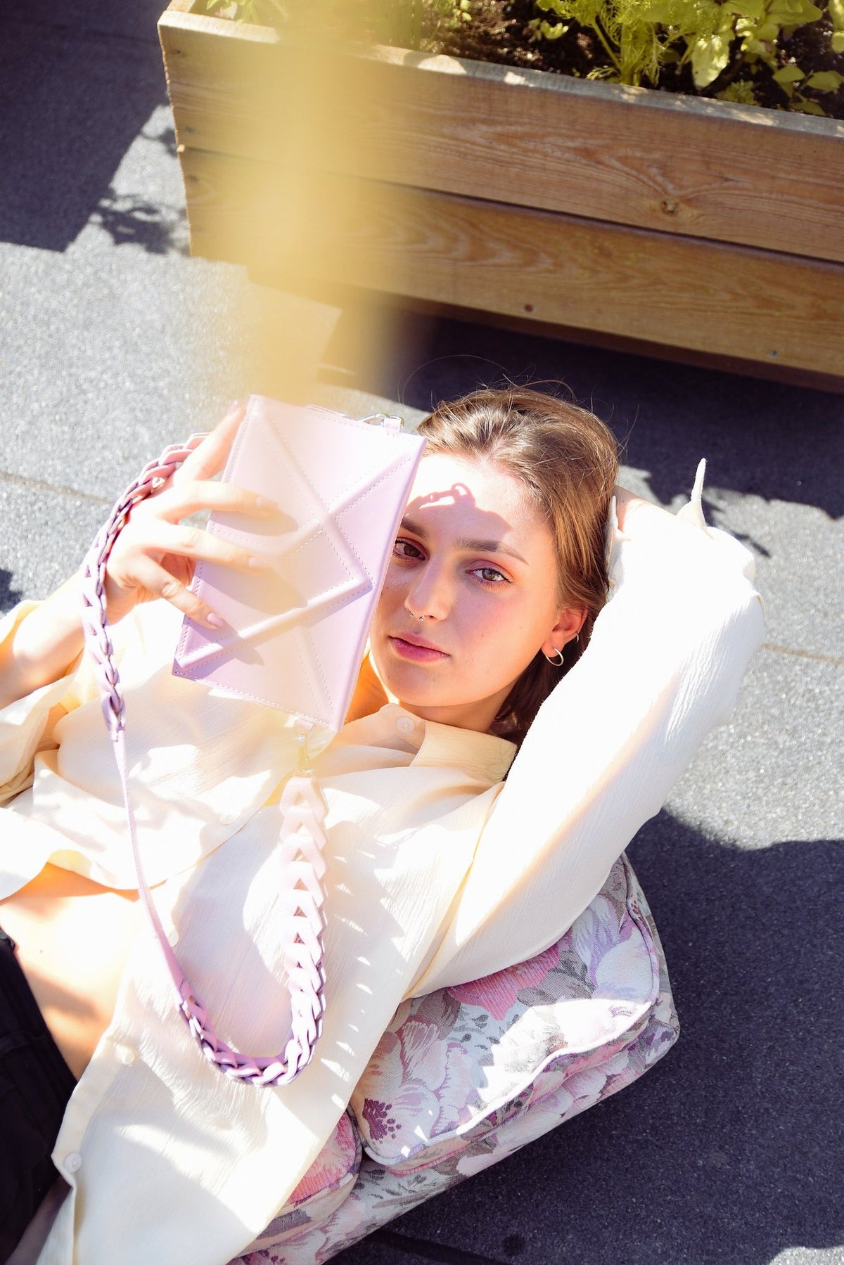 5. Women's pink FACET Clutch by Gerda Retter with Venice strap, held by model lying down