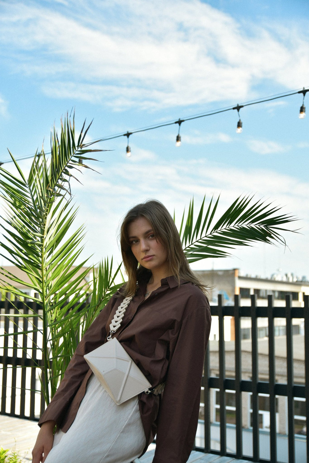 3. Women's beige FACET Clutch by Gerda Retter with Venice strap, worn crossbody in outdoor setting