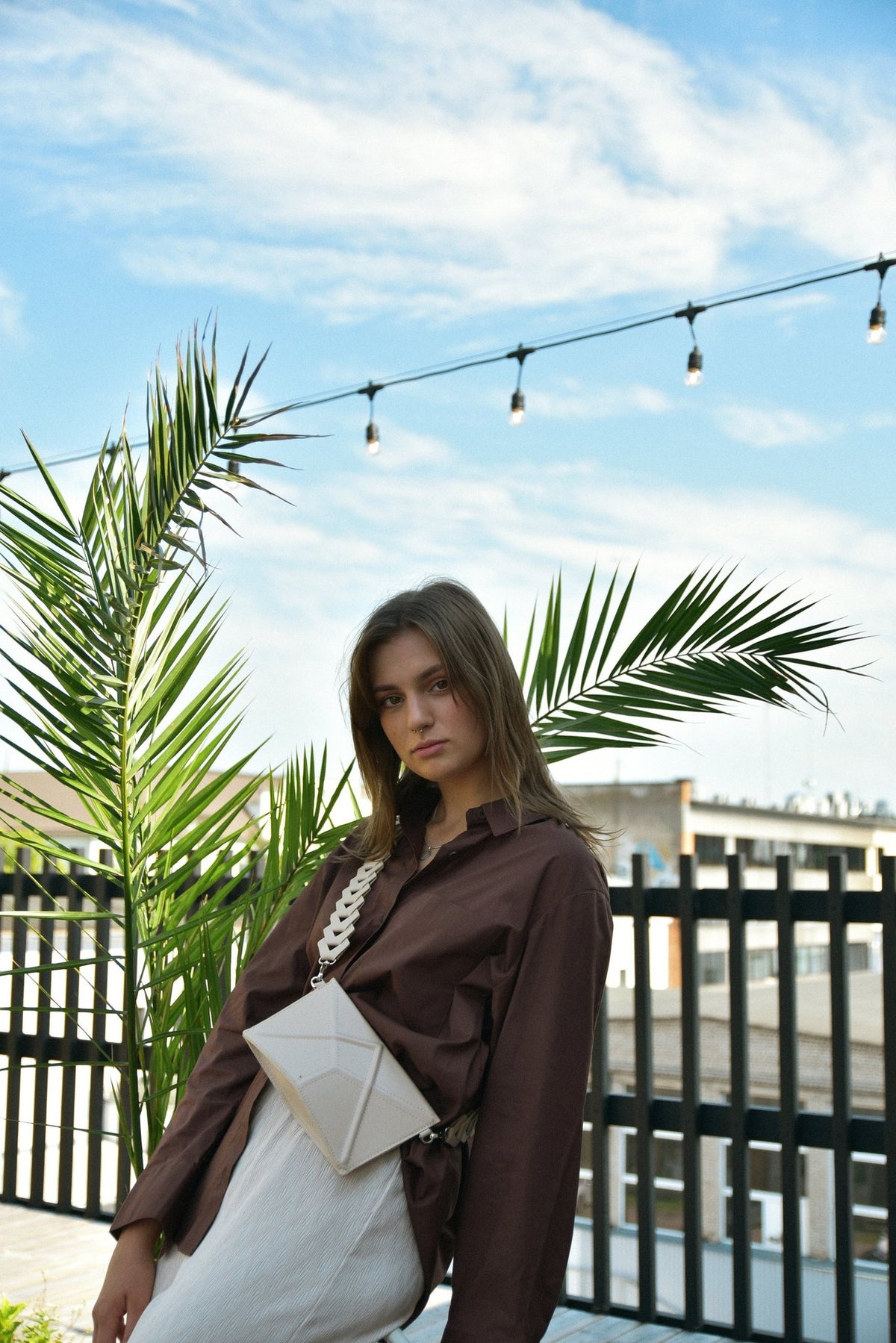 3. Women's beige FACET Clutch by Gerda Retter with Venice strap, worn crossbody in outdoor setting