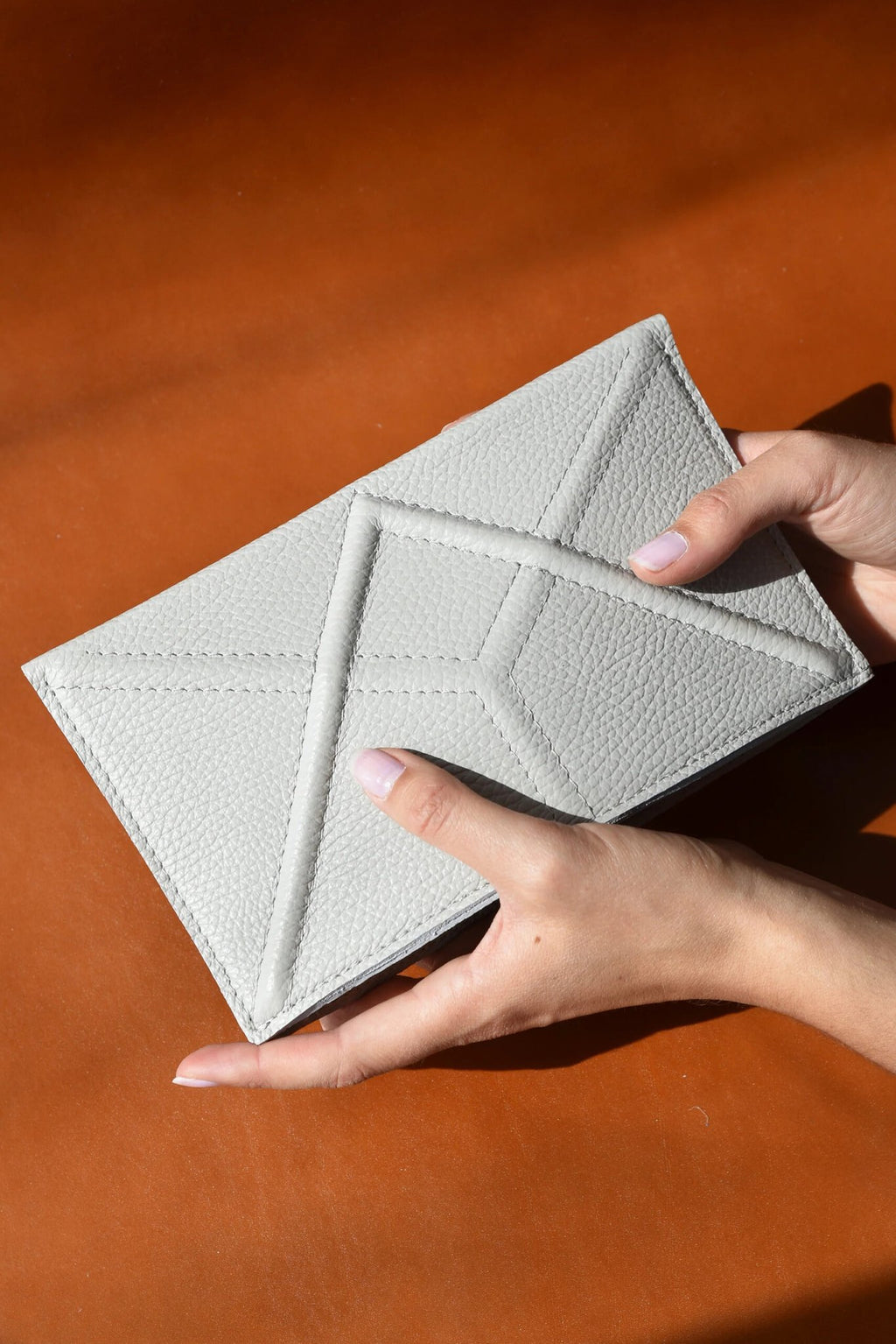 1. Women's hands holding Gerda Retter Design FACET Clutch in light grey Spanish leather, showcasing geometric pattern
