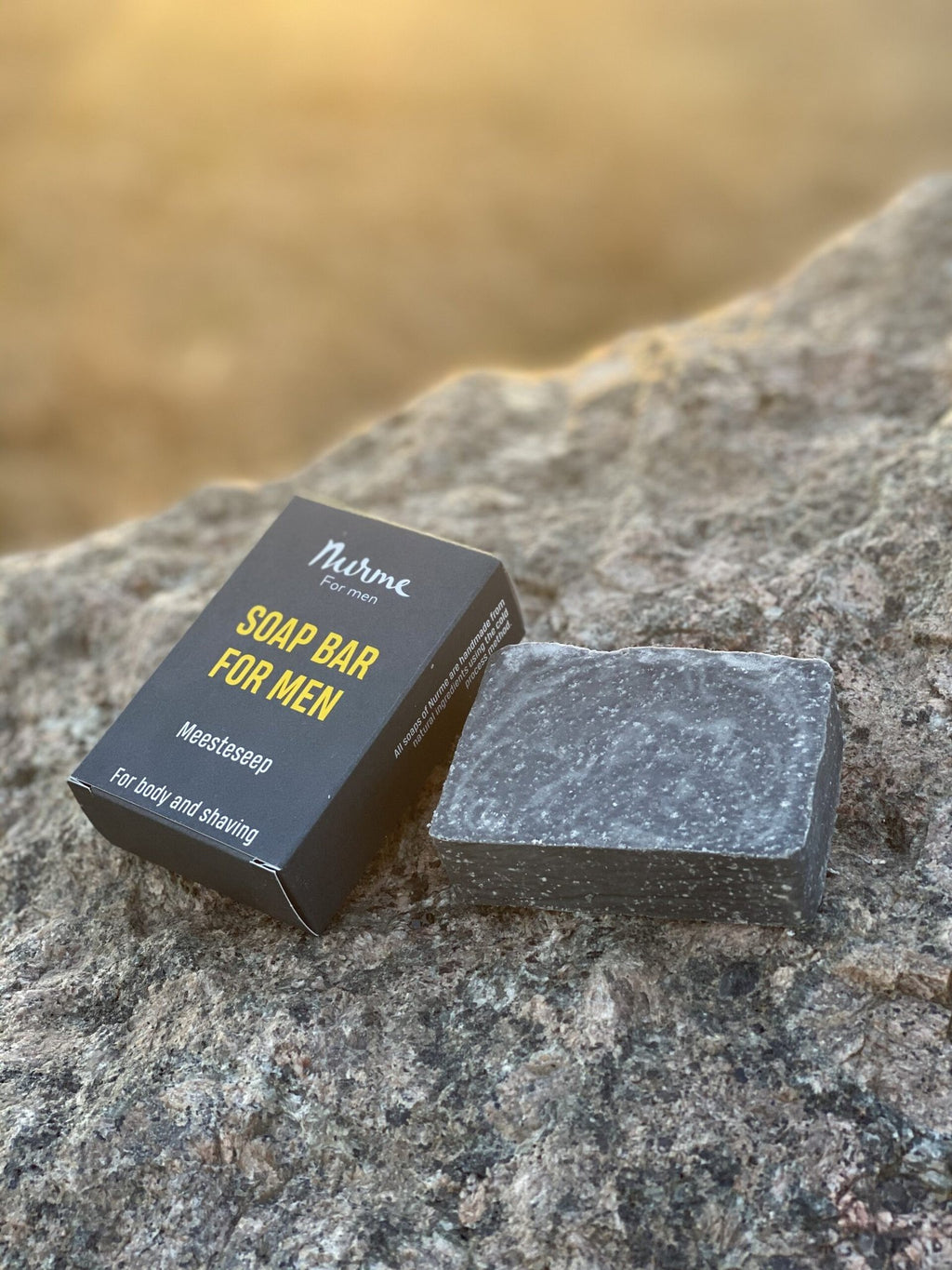 1. Nurme men's soap bar with dark packaging and grey soap bar on a rock in natural outdoor setting