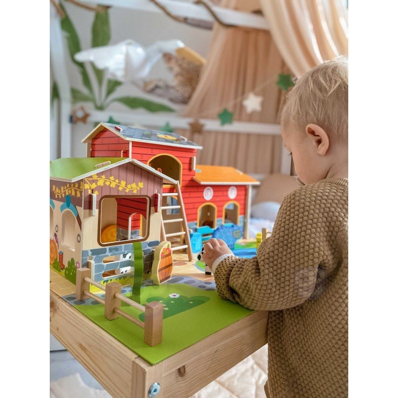 1. Child playing with Woopie Green Mega Farm set on a table, featuring barn and animal figurines in a nursery