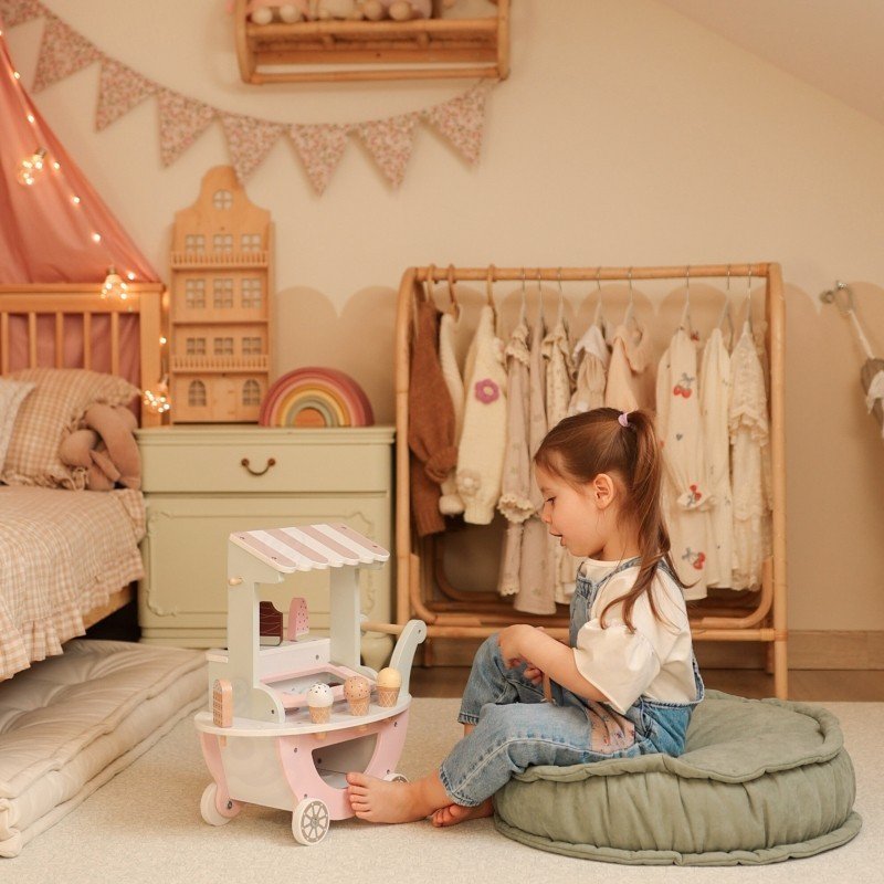 1. Child sitting on cushion playing with pastel wooden ice cream cart in a decorated playroom